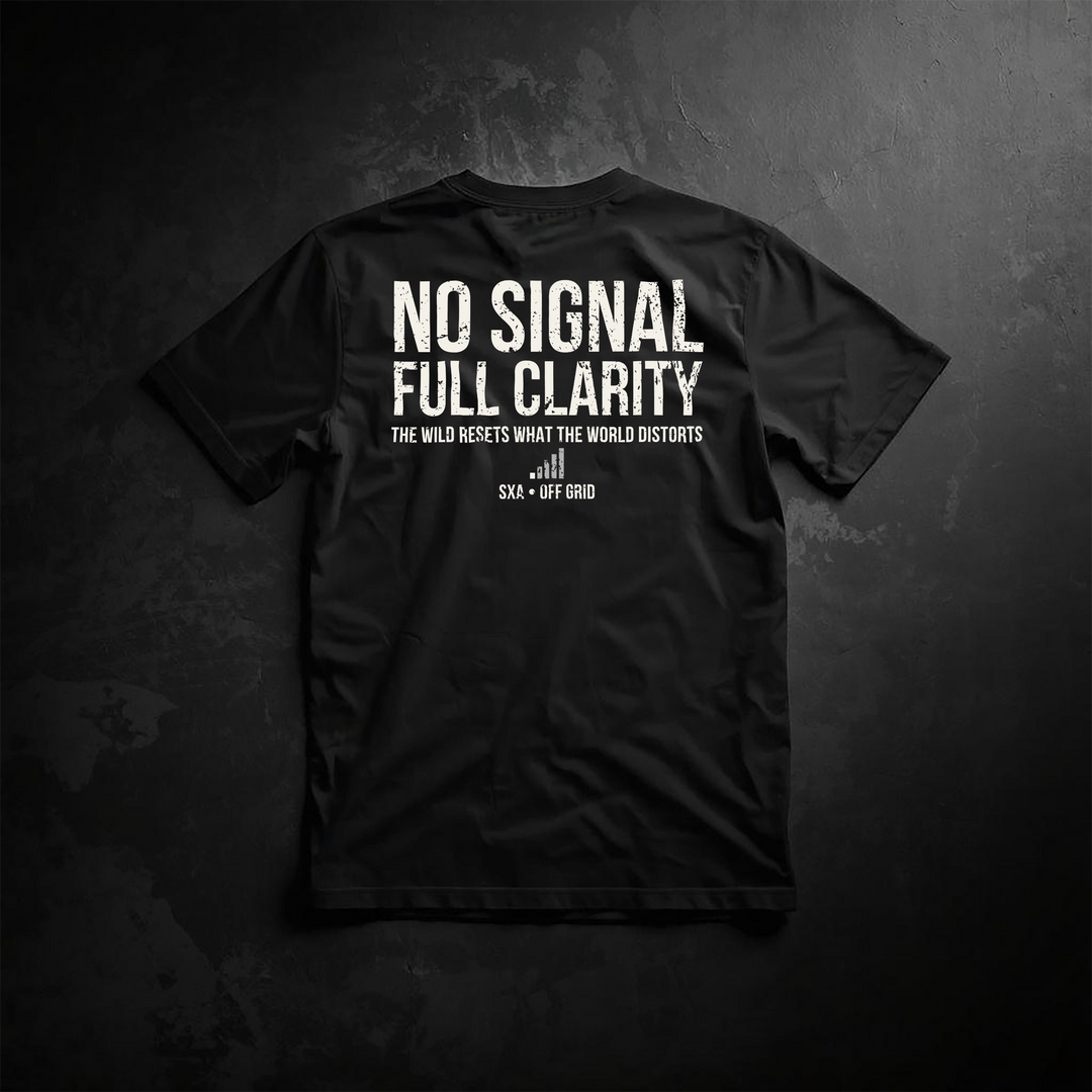 An image of the back of a black t-shirt featuring a distressed white typography design. The main text reads "NO SIGNAL FULL CLARITY" in a weathered, bold sans-serif font. Below it, a smaller tagline states, "THE WILD RESETS WHAT THE WORLD DISTORTS," positioned above a minimalist cell signal bar icon with a strike-through. The brand branding "SXA • OFF GRID" is printed at the bottom. The shirt is laid flat on a dark, textured stone background, catering to off-grid living, camping, and outdoor adventure enthu