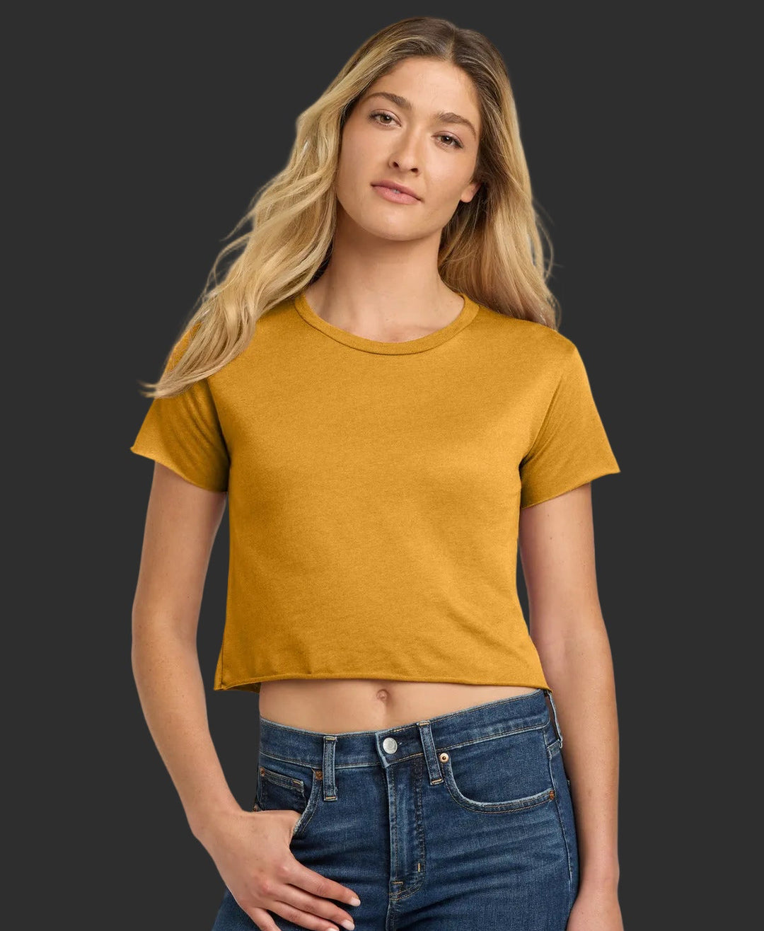 Woman wearing a mustard yellow crop top and blue jeans on a white background